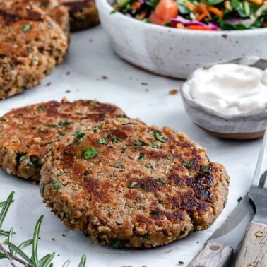 completed white bean burger patties on a white surface with ingredients in the background