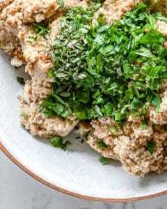 process of adding herbs to white bean mixture in bowl