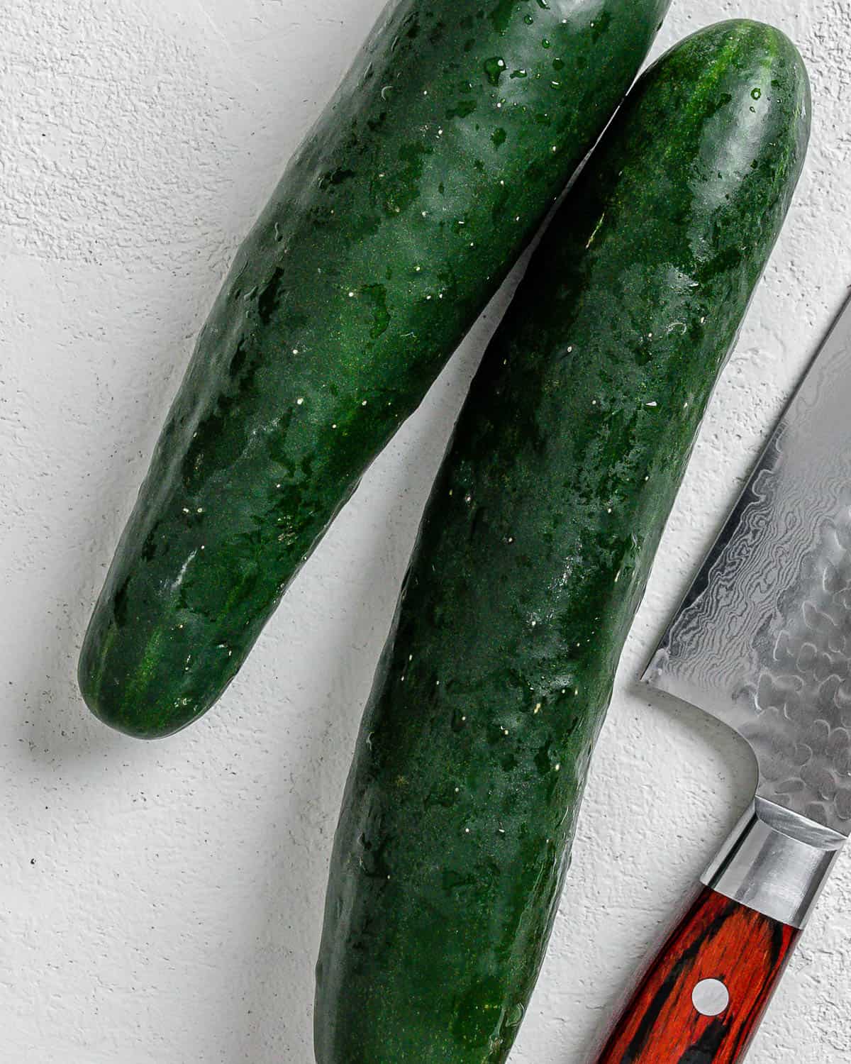 two cucumbers and a knife against a white surface