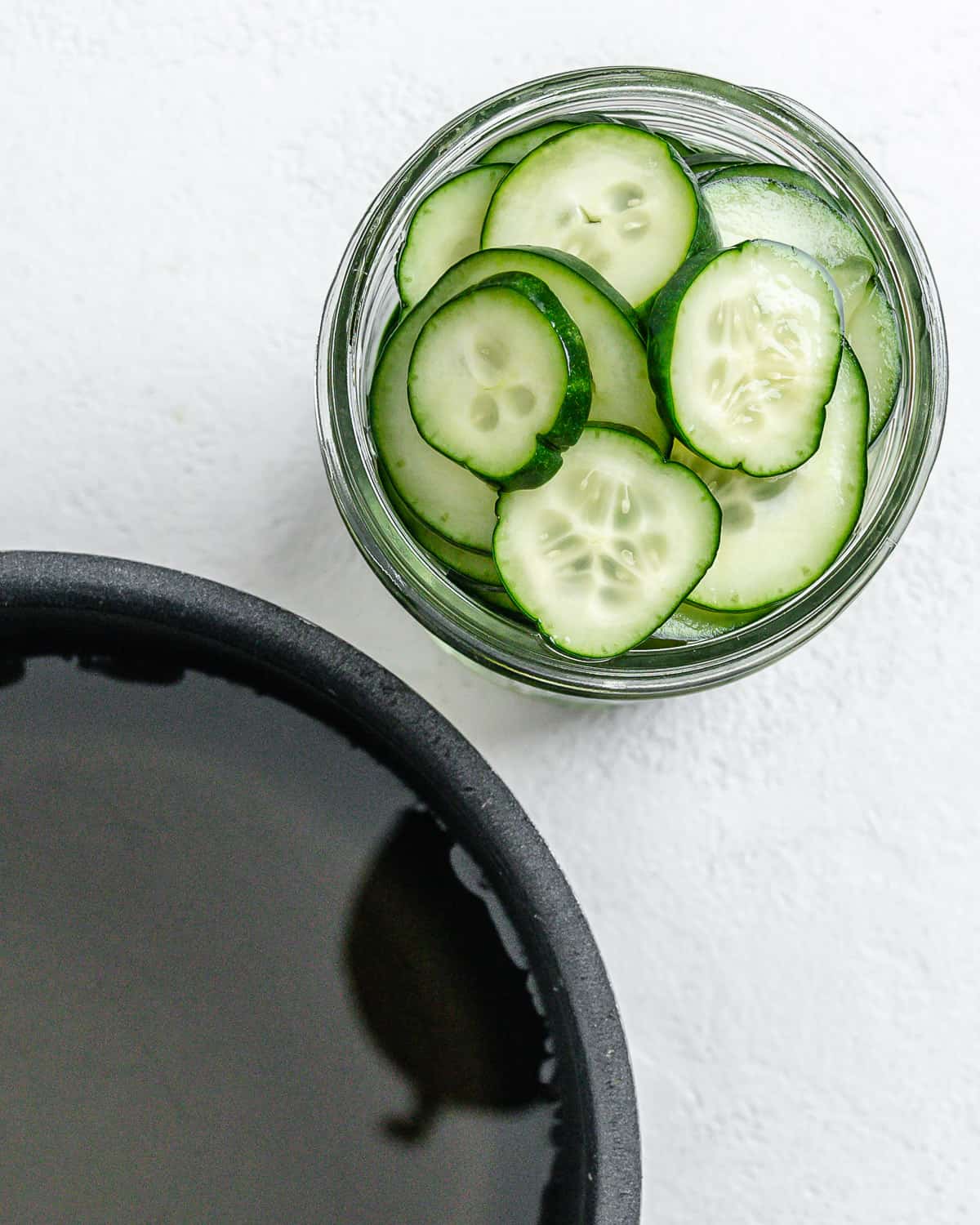 small bowl of cucumbers alongside a black pan against a white surface