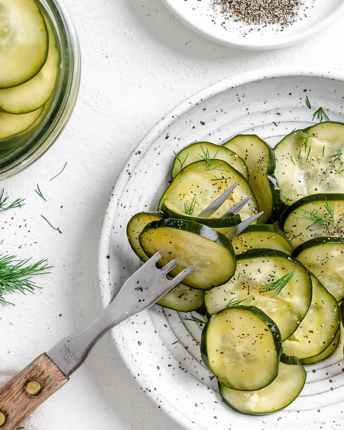 completed Marinated Cucumber Salad on a white plate with a frok in two pieces against a white surface