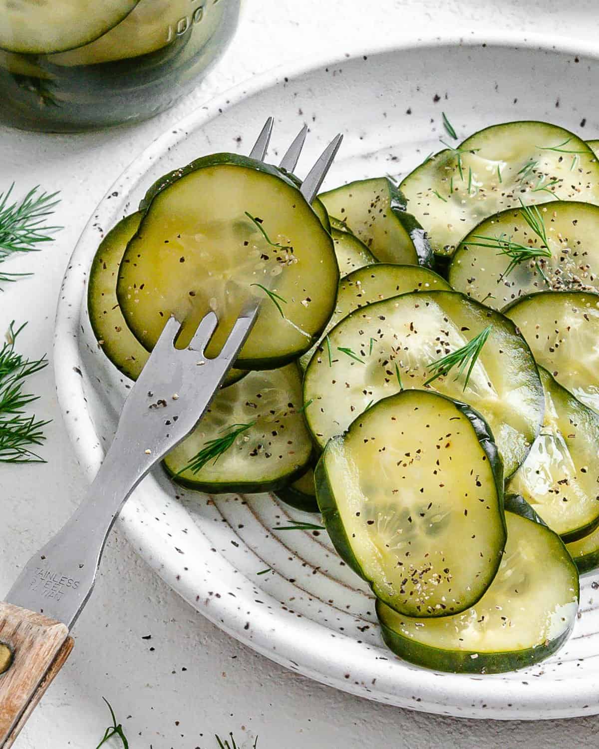 completed Marinated Cucumber Salad on a white plate with a frok in two pieces against a white surface
