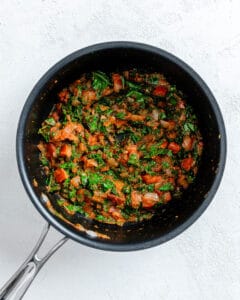 process of sauce being cooked in a black skilled against a black background