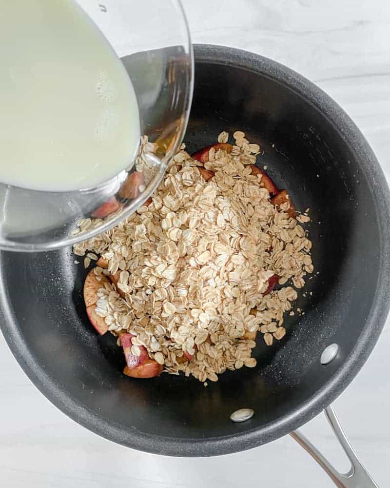 Plant-based milk being poured into a saucepan of oats and cinnamon apples.