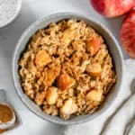 finished apple cinnamon oatmeal in a bowl with ingredients in a white background