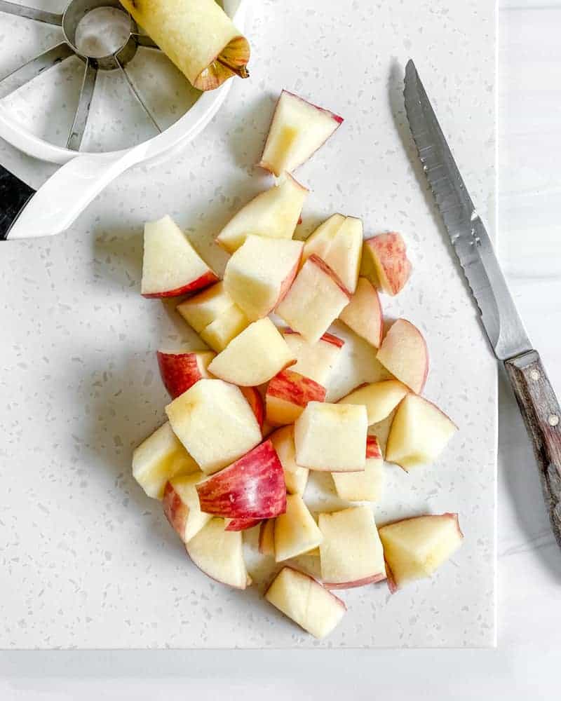A cored apple cut into small cubes on a white cutting board.