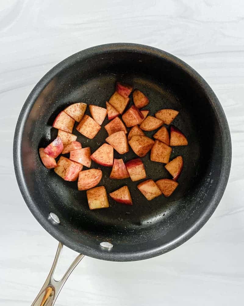 Golden sautéed cinnamon apple cubes in a black saucepan.