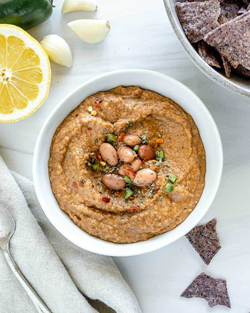 Bowl of pinto bean dip on a white cutting board with pinto beans as a garnish.
