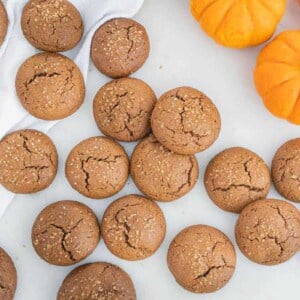 several pumpkin molasses cookies with pumpkin in the background against a white surface