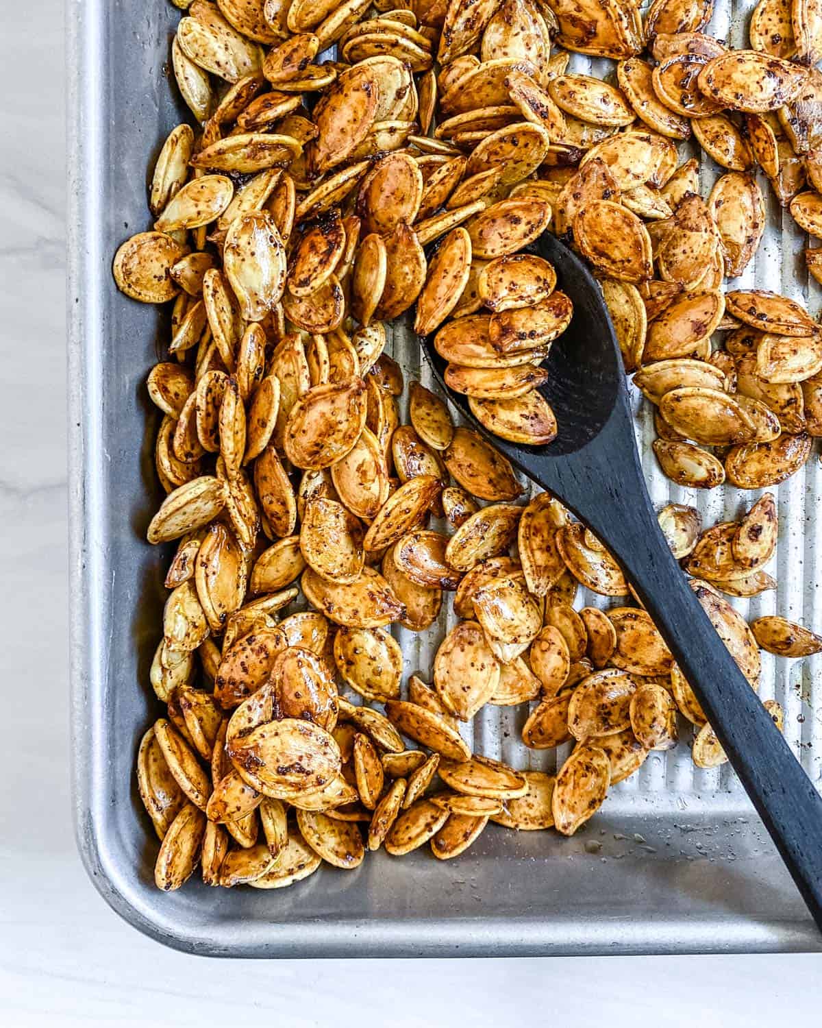 completed roasted spicy pumpkin seeds being mixed on. baking tray