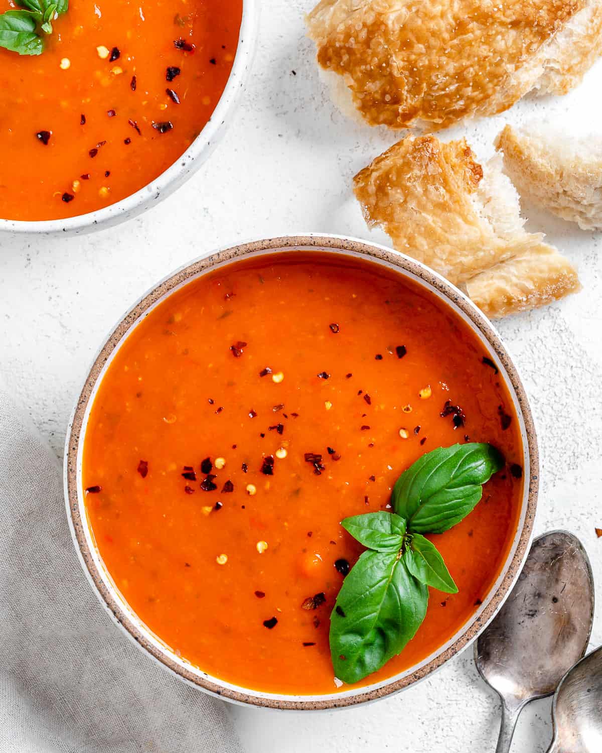 completed Tomato Basil Soup in a bowl against a light surface with ingredients in the background