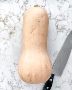 raw butternut squash with knife against a white marble background
