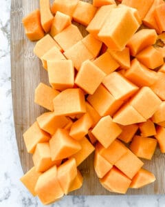 cubed butternut squash with knife against a white marble background