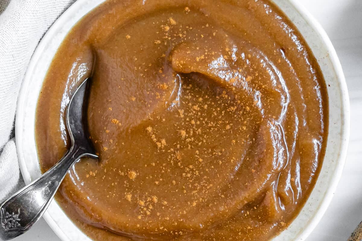 finished homemade caramel sauce in a white bowl with a spoon and dates in the background