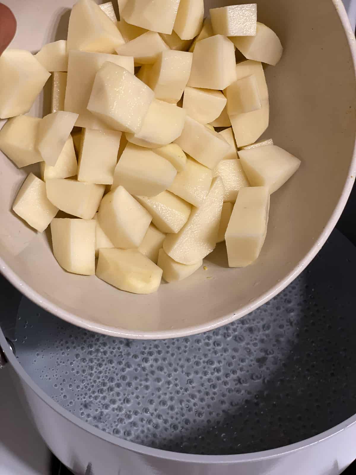 cubed potatoes in a bowl above a pan