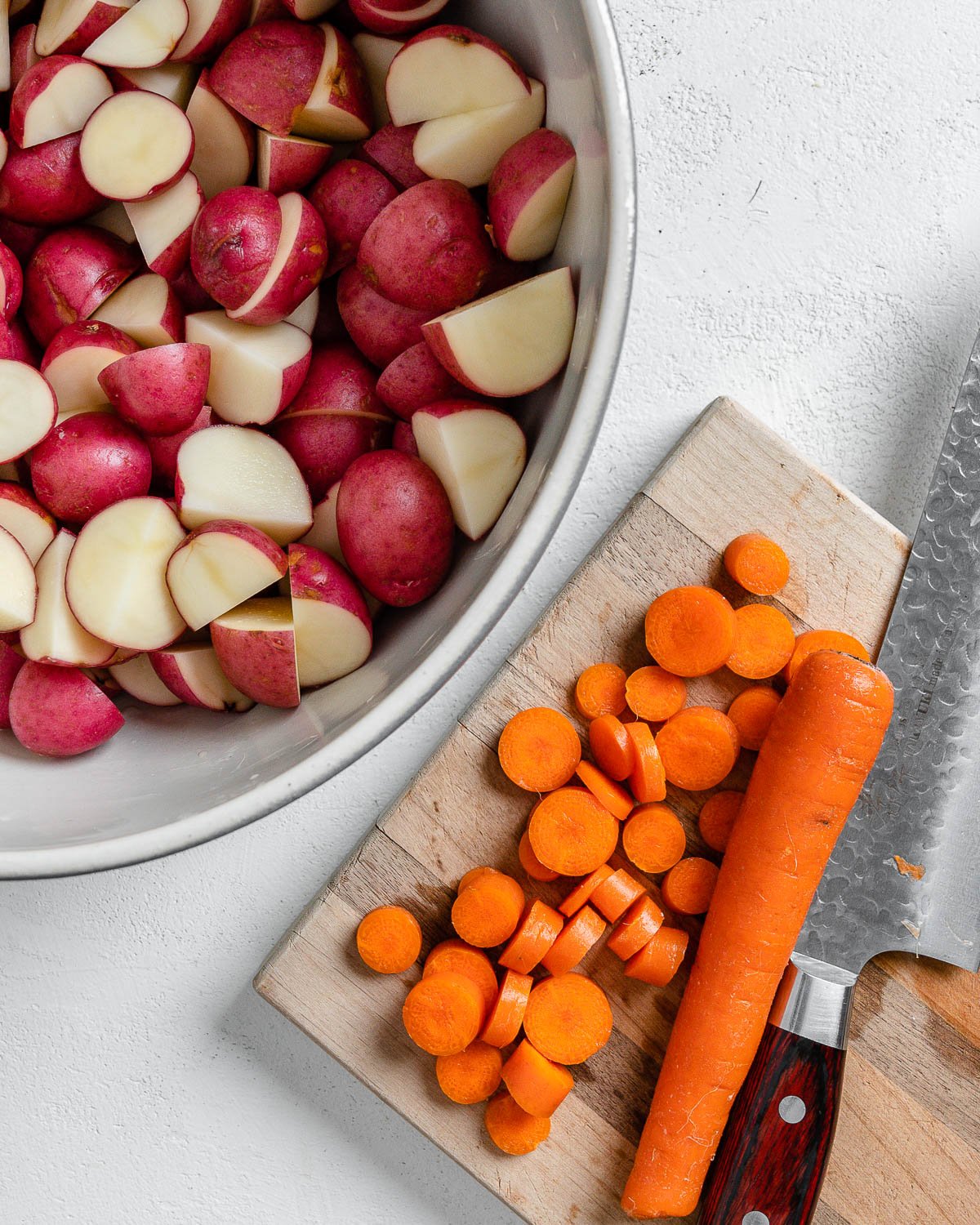process of cutting carrots on a brown cutting board alongside bowl of potatoes