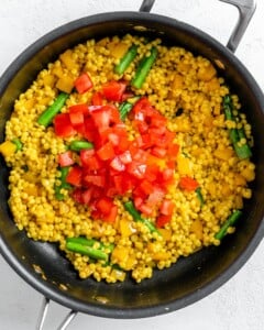 process of adding tomatoes to couscous veggie mix in pan