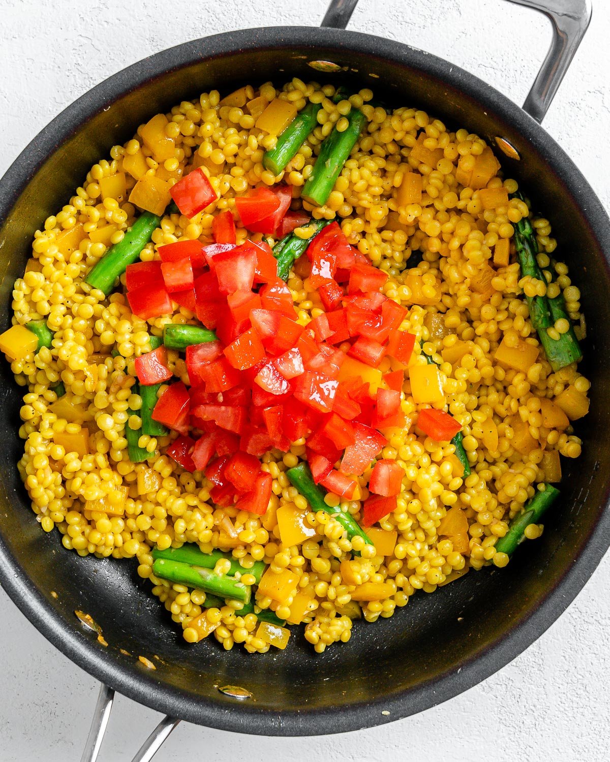 process of adding tomatoes to couscous veggie mix in pan