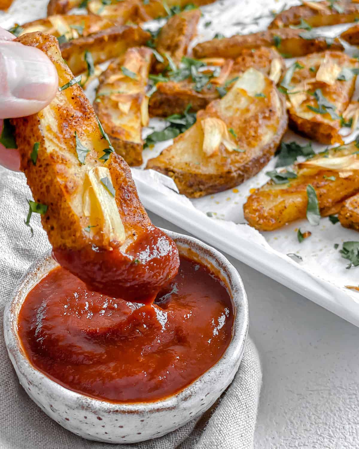 close up of one potato wedge being dipped into bowl of ketchup