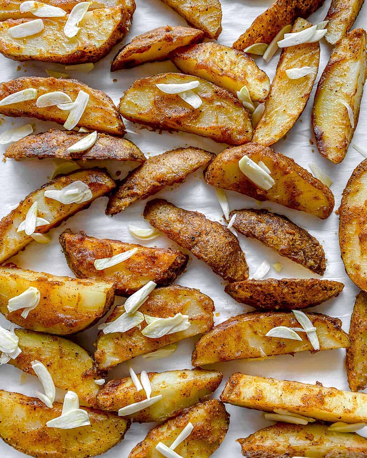 process of adding additional ingredients to Oven Baked Garlic Parsley Fries scattered on a baking tray