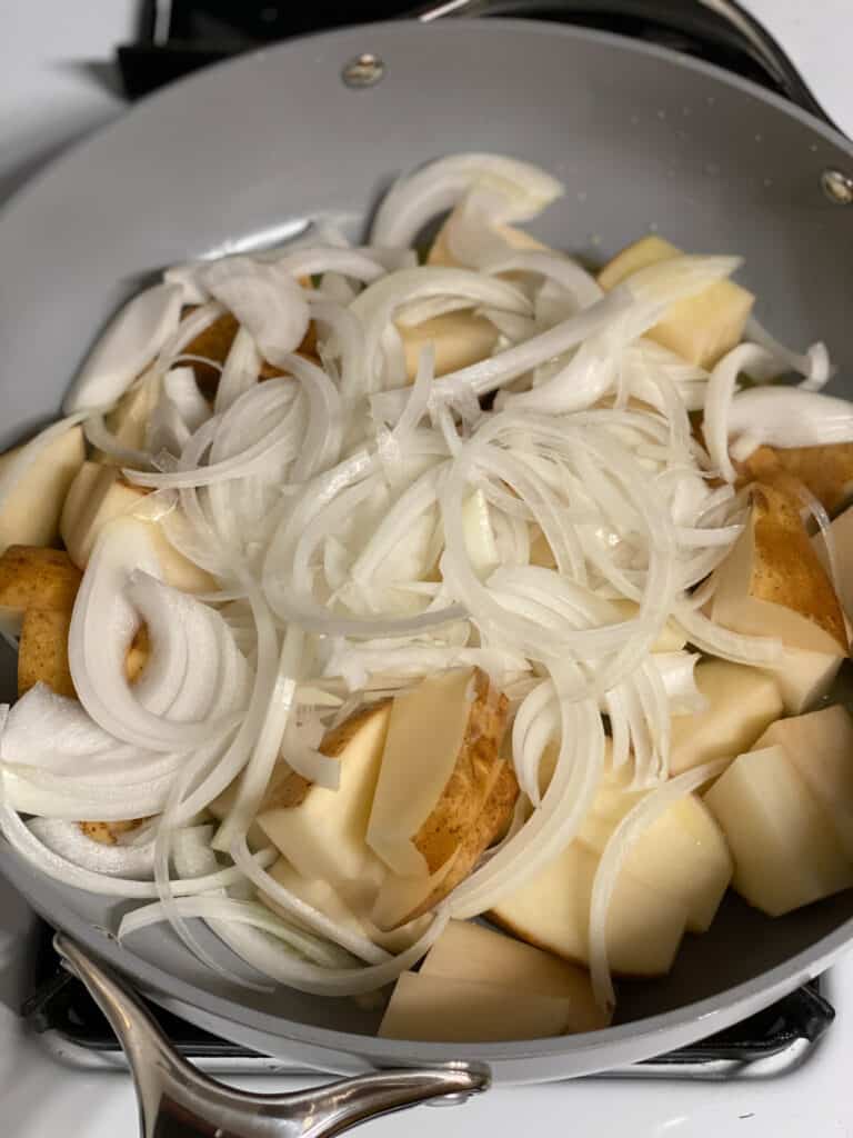 process shot of mixing in onions with potatoes in pan
