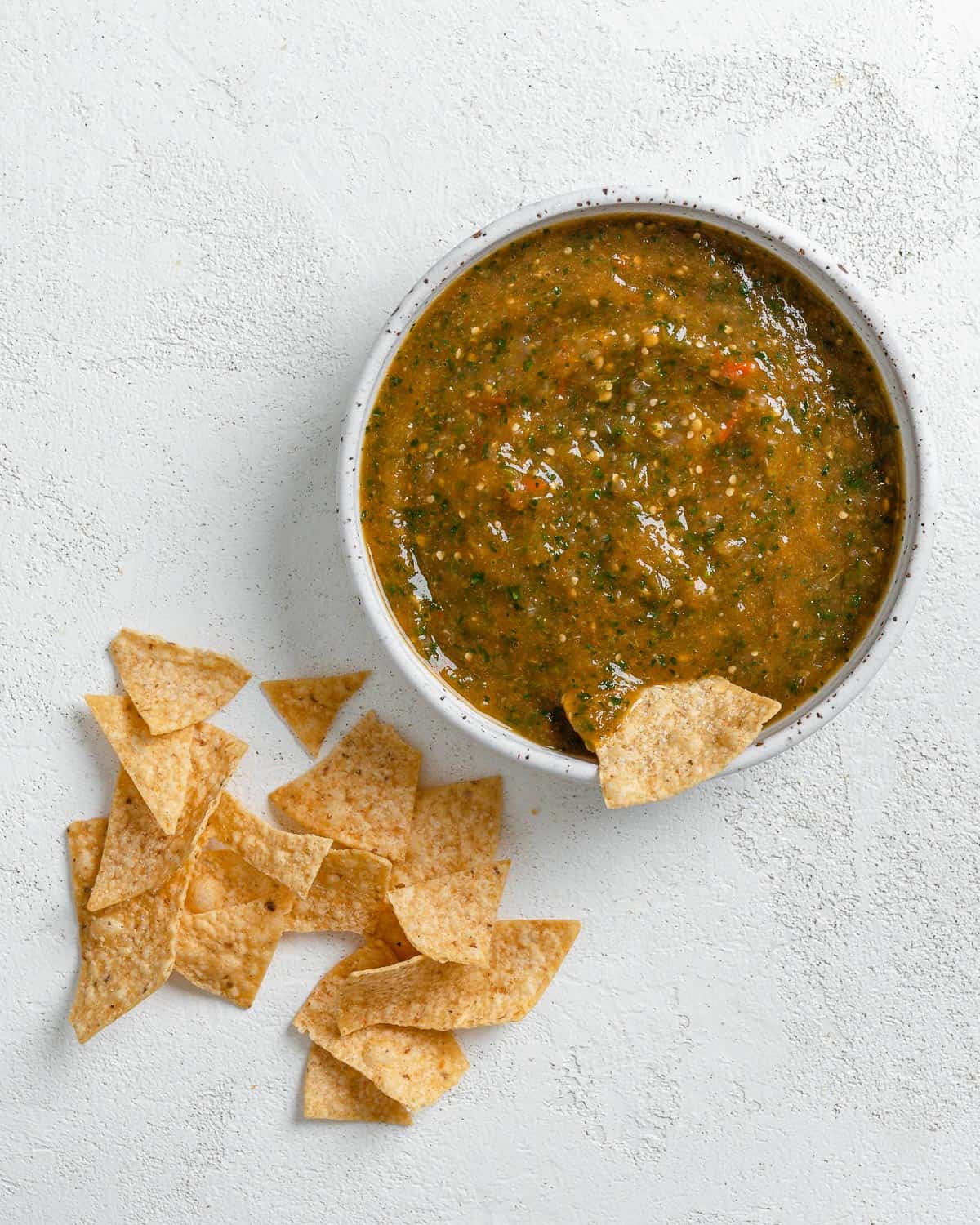 completed Stovetop Tomatillo Salsa in a bowl with a chip being dipped in it and chips scattered on the side