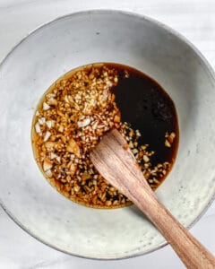 process of mixing garlic and tamari sauce in white bowl with wooden spoon