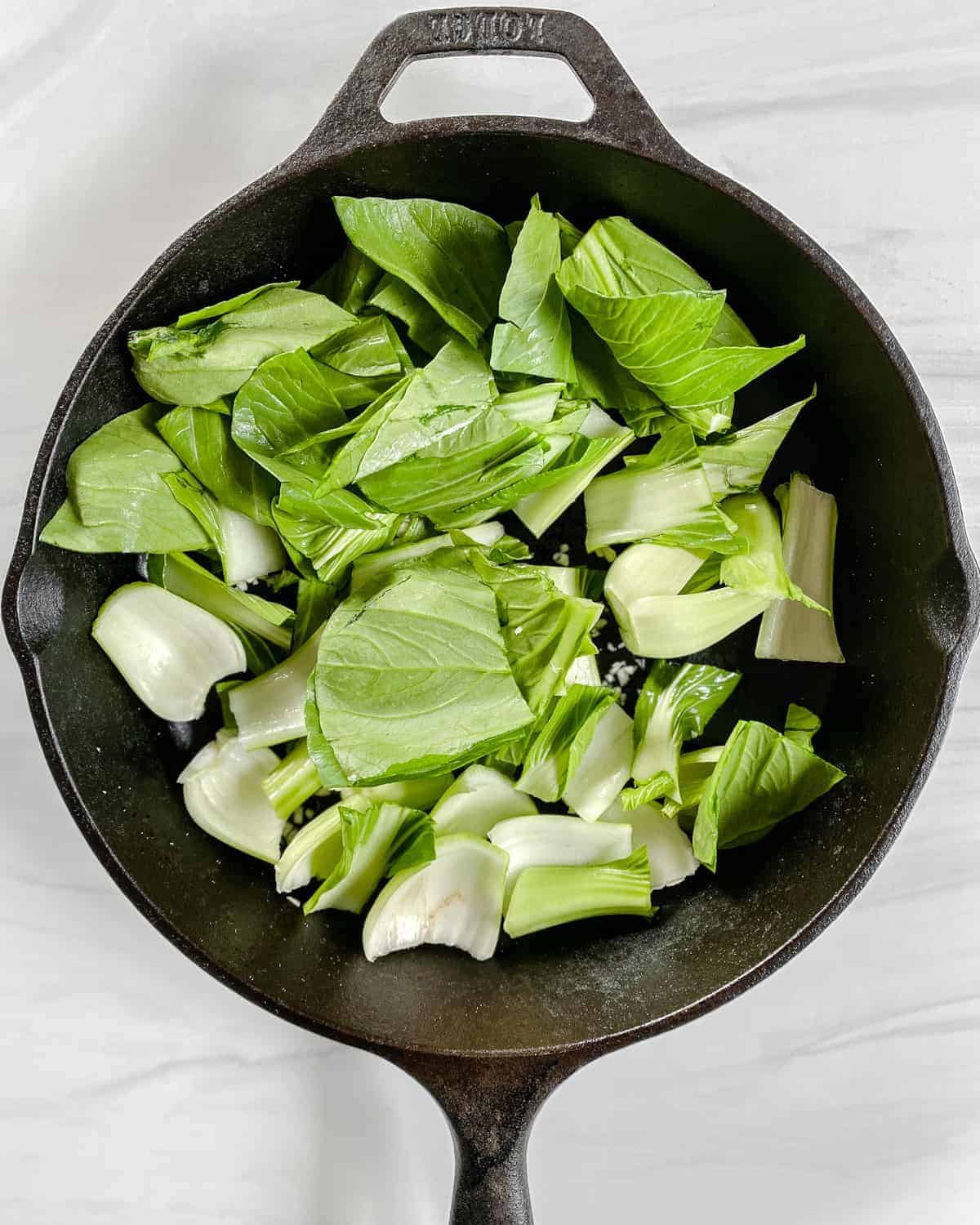 process of adding greens to black pan against white background