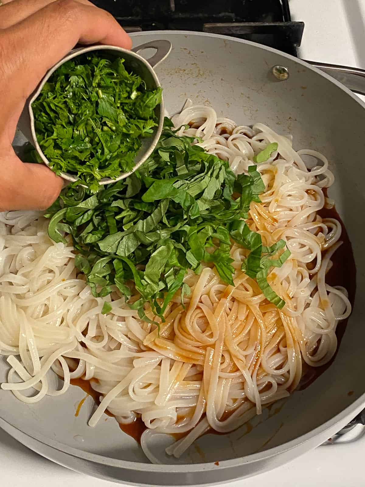 process of adding cilantro to pan of noodles