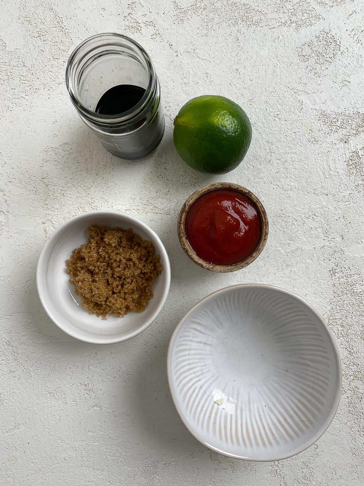 ingredients for sauce measured out in bowls against a white surface