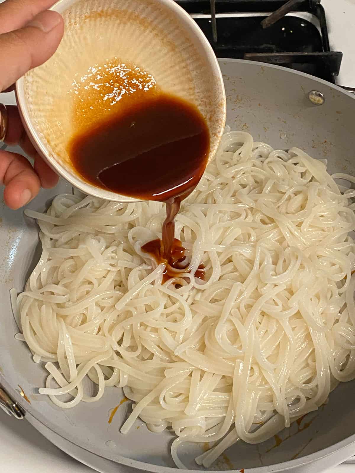 process of adding additional sauce on top of rice noodles in pan