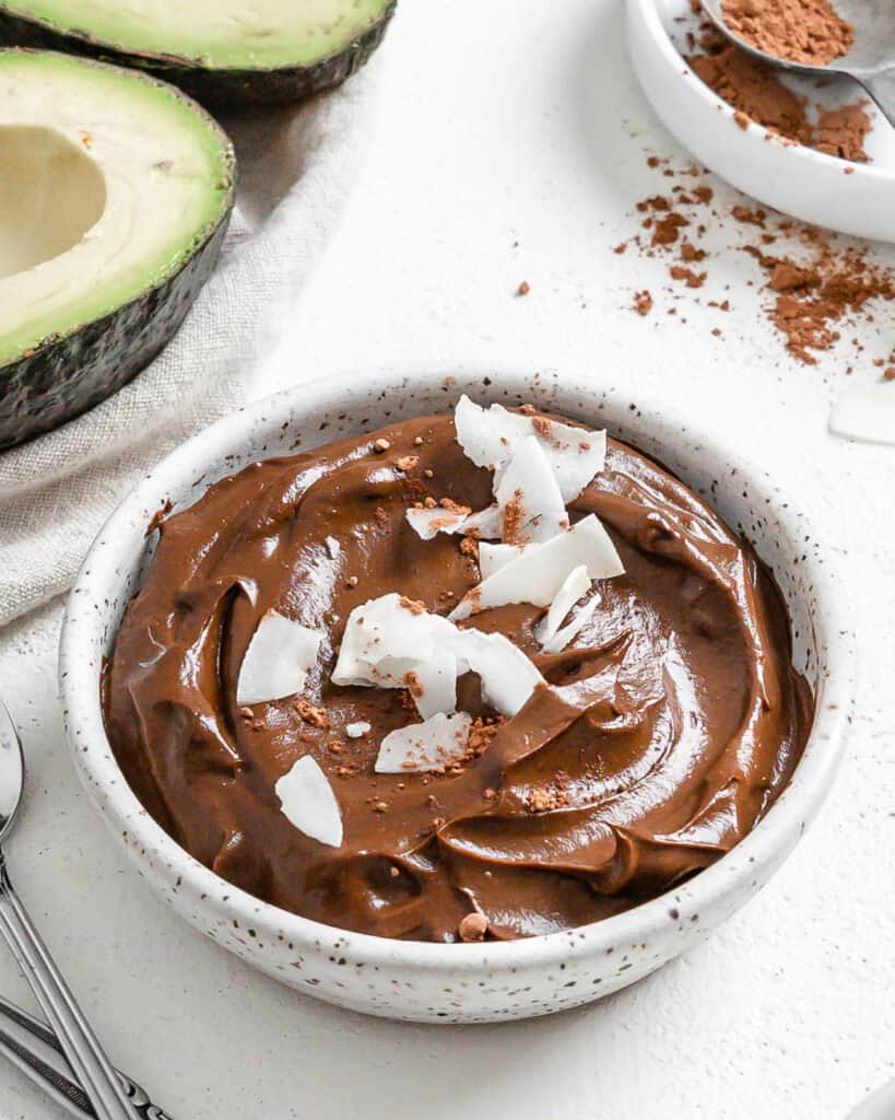 completed Chocolate Avocado Pudding in a white bowl with avocados in the background