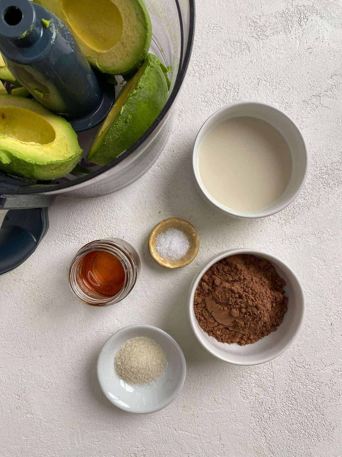 ingredients for Chocolate Avocado Pudding against a white background with avocados in a bowl