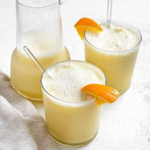 two completed Easy Orange Julius Smoothies in glass cups with a pitcher in the background