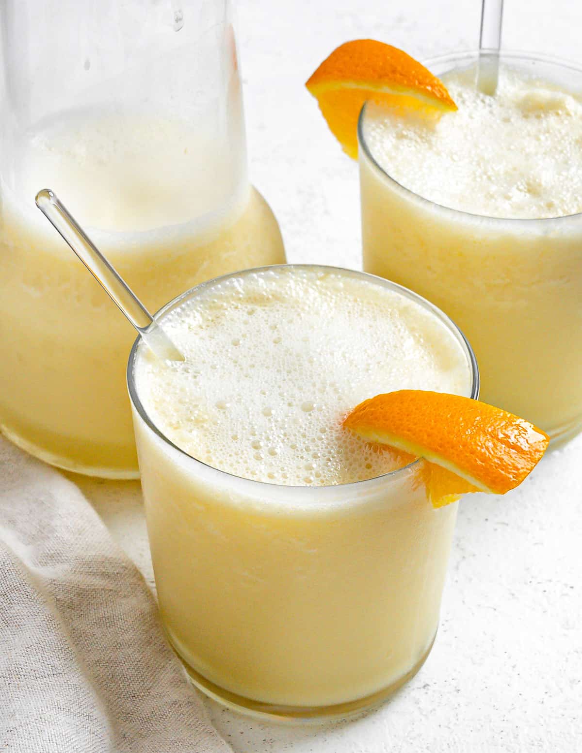 two completed Easy Orange Julius Smoothies in glass cups with a pitcher in the background