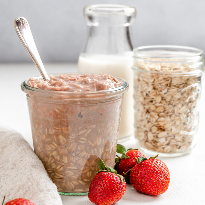 completed Vegan Strawberry Overnight Oats in two glass jars with strawberries in the forefront on a white surface
