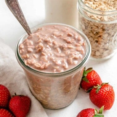 completed Vegan Strawberry Overnight Oats in two glass jars with strawberries in the forefront on a white surface