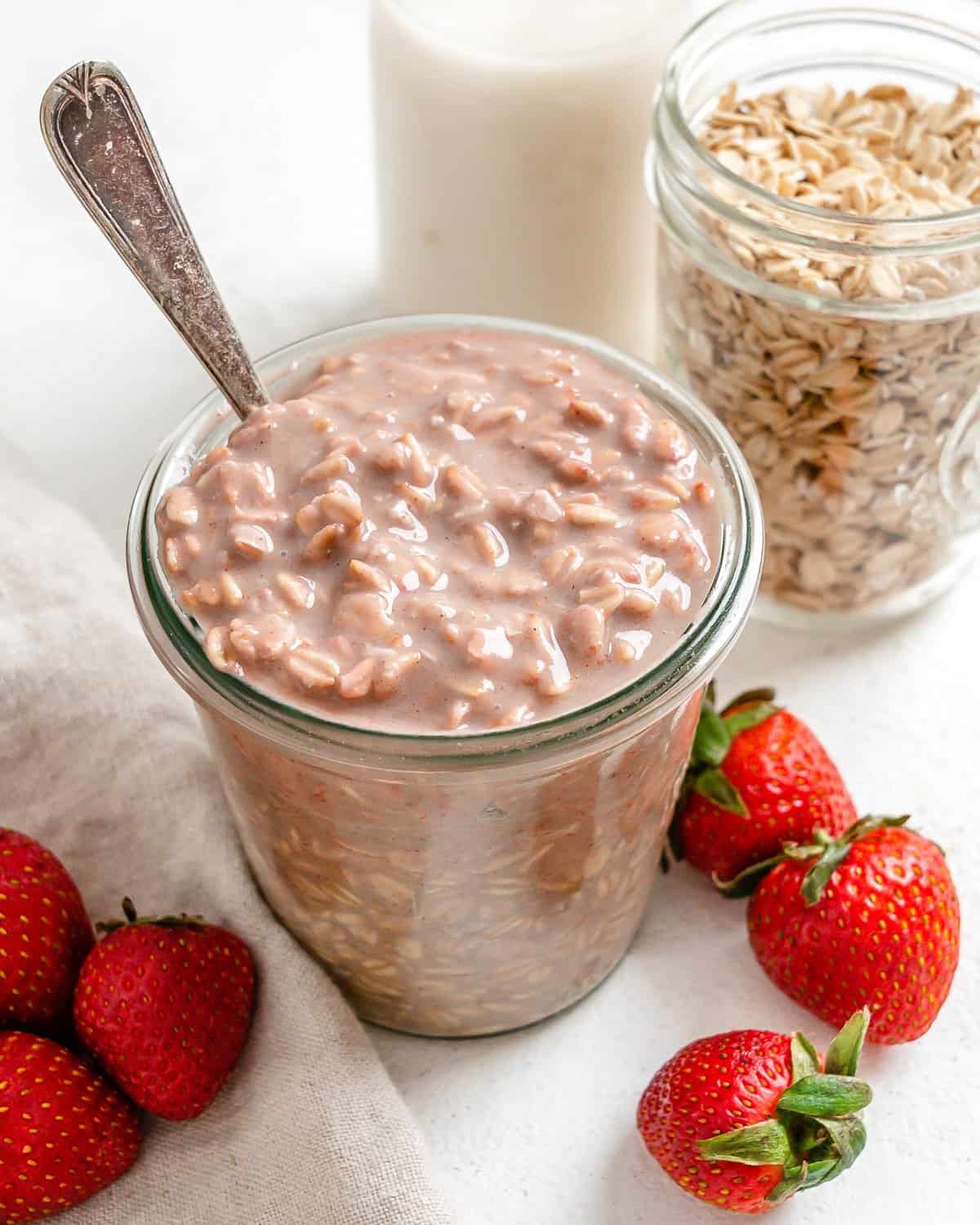 completed Vegan Strawberry Overnight Oats in two glass jars with strawberries in the forefront on a white surface