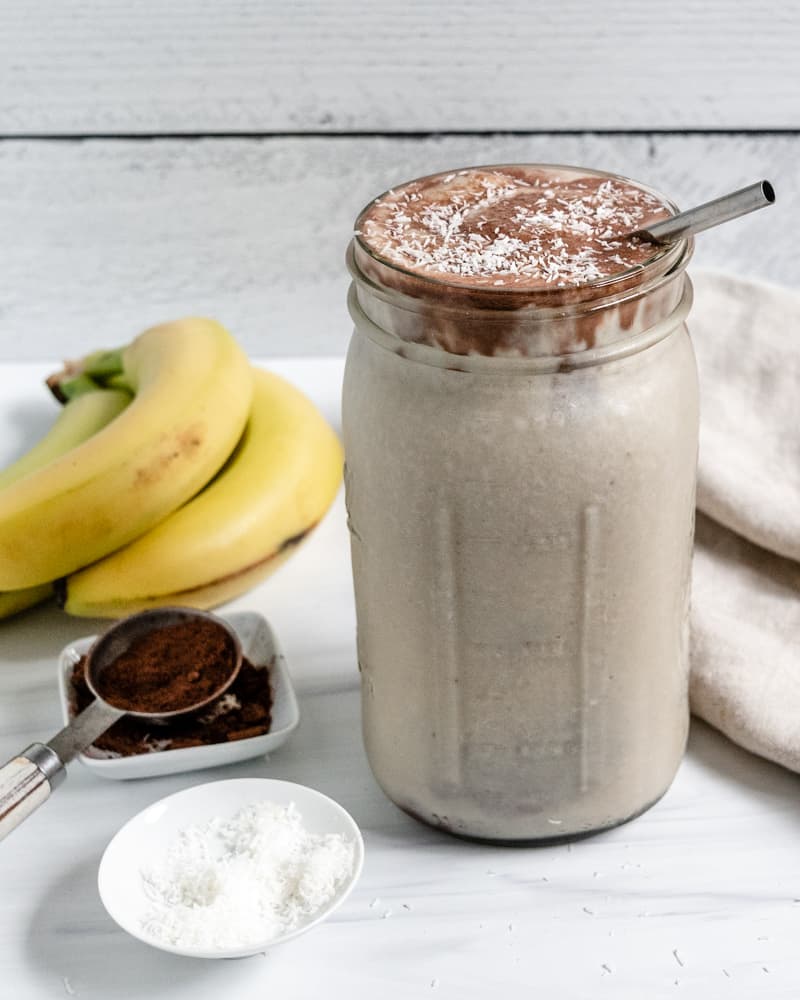completed C،colate Peanut Butter Banana Smoothie in a jar with ingredients in the background