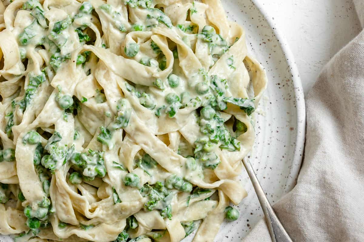 completed Dairy Free Alfredo Sauce with Kale and Peas plated on a white plate against a white surface