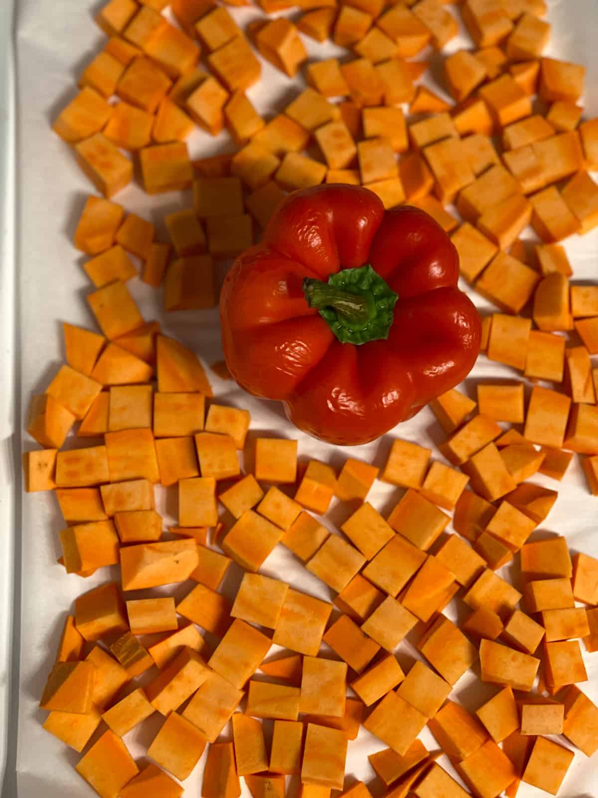 cubed sweet potato alongside a red pepper on a baking tray