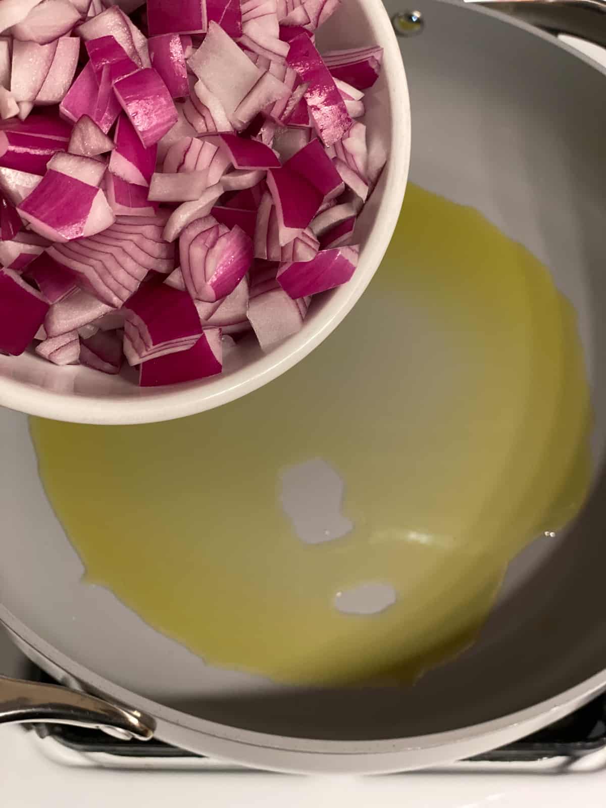 process shot of pouring diced onions to pan of oil