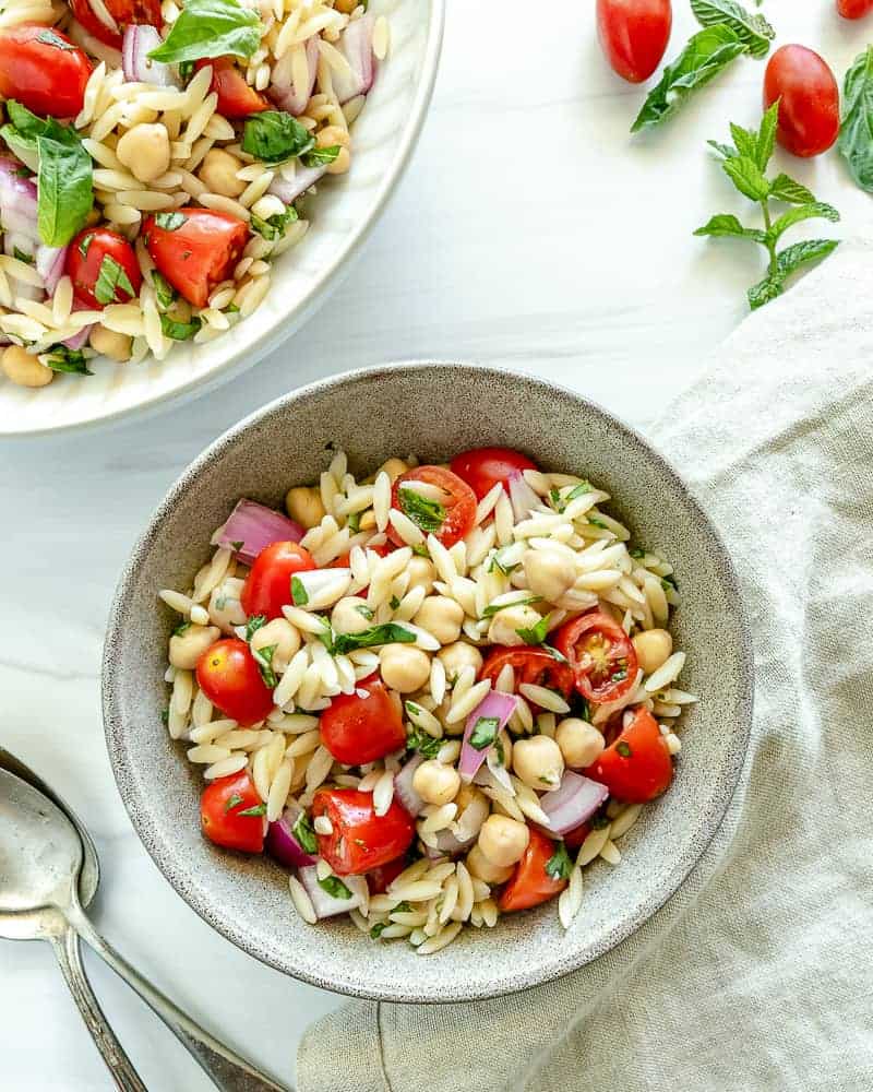 finished orzo chickpea salad in a white bowl with ingredients in a white background