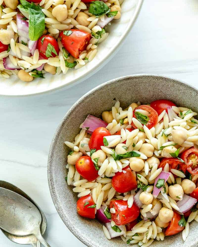 finished orzo chickpea salad in a white bowl with ingredients in a white background