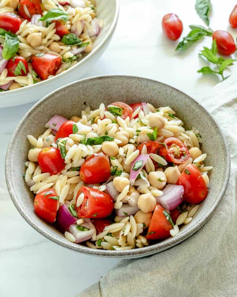 finished orzo chickpea salad in a white bowl with ingredients in a white background