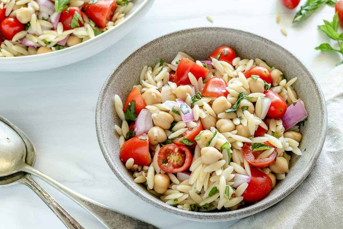 finished orzo chickpea salad in a white bowl with ingredients in a white background