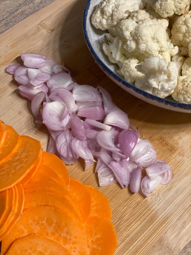 sweet potatoes, onions, and cauliflower sliced and chopped on a cutting board