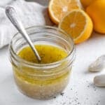 completed lemon dressing in a glass jar with a spoon in it and ingredients in the white background