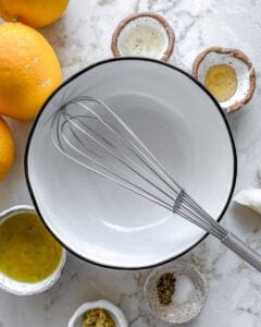ingredients for lemon dressing placed around a white bowl and whisk