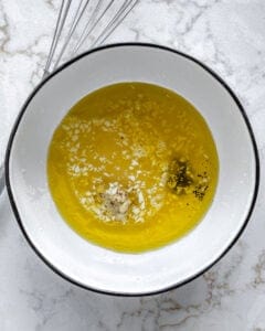 lemon dressing ingredients added to white bowl against white background
